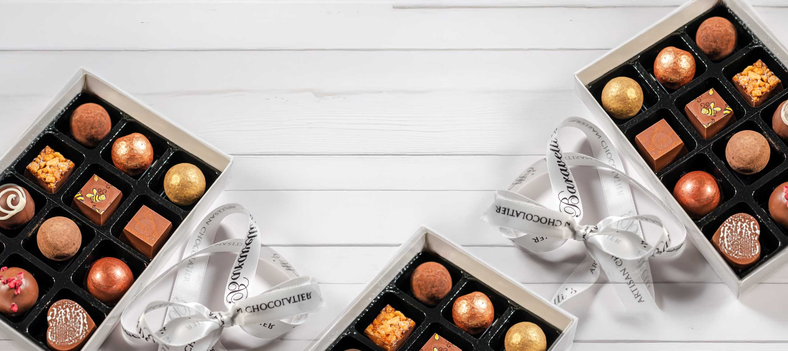 Two open boxes of Baravelli's truffles tied with printed ribbon on a white board